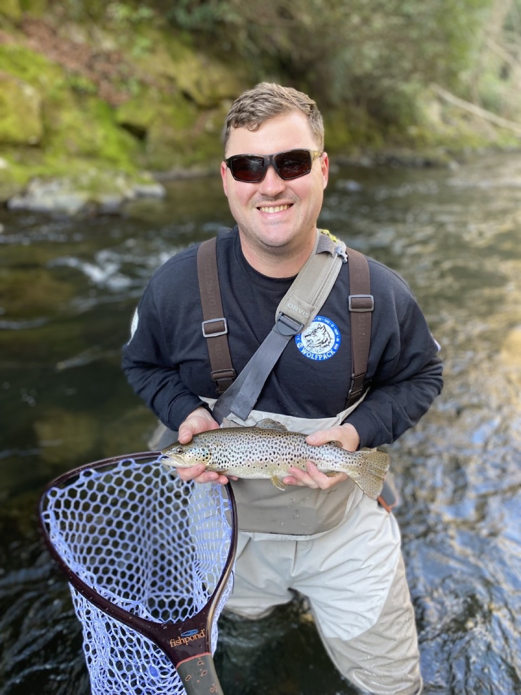 Angler with a brown trout and net on a green Blue Ridge river